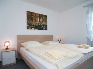 A double bed with a headboard, two bedside tables with lamps, a wall-mounted painting of a forest, and a window with a curtain. - Reriker Straße 06b Whg. RER6b-2 .. - Reriker Str. 6b Whg. RER6b-02 (Kühlungsborn)