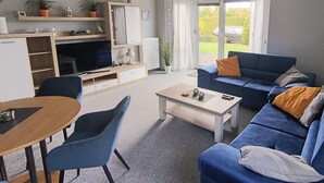 A living room with a sofa, a coffee table, a TV, and a dining area with chairs. - Reriker Straße 06b Whg. RER6b-2 .. - Reriker Str. 6b Whg. RER6b-02 (Kühlungsborn)