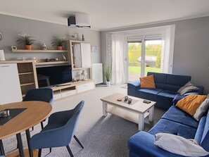A living room with a sofa, a coffee table, a TV, and a dining area with chairs. - Reriker Straße 06b Whg. RER6b-2 .. - Reriker Str. 6b Whg. RER6b-02 (Kühlungsborn)
