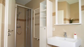 A bathroom with a glass-enclosed shower, a white sink with a mirror above it, and a white cabinet with shelves. - Reriker Straße 06b Whg. RER6b-2 .. - Reriker Str. 6b Whg. RER6b-02 (Kühlungsborn)