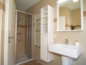A bathroom with a glass-enclosed shower, a white sink with a mirror above it, and a white cabinet with shelves. - Reriker Straße 06b Whg. RER6b-2 .. - Reriker Str. 6b Whg. RER6b-02 (Kühlungsborn)