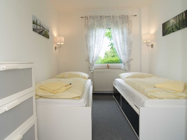 A bedroom with two beds, a window with lace curtains, wall-mounted lamps, and a radiator. - Reriker Straße 06b Whg. RER6b-2 .. - Reriker Str. 6b Whg. RER6b-02 (Kühlungsborn)