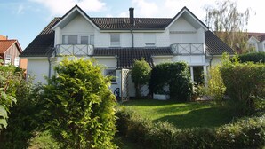 A two-story house with a sloped roof, a front porch, and a small garden area. - Reriker Straße 06b Whg. RER6b-2 .. - Reriker Str. 6b Whg. RER6b-02 (Kühlungsborn)