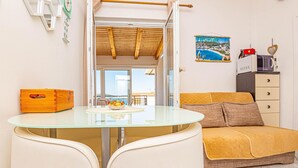 A compact living space with a glass table, a sofa, a wooden chest of drawers, and a view of the outdoors.