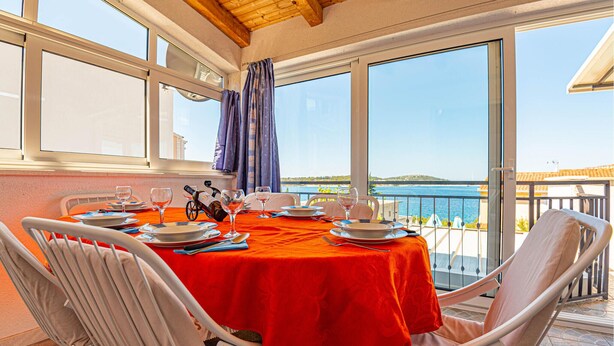A dining table set for four with a red tablecloth, white chairs, and a view of the sea.