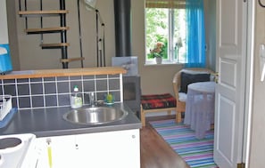 A compact kitchen with a sink, a small window with a view of greenery, and a chair with a blanket. - 1 bedroom amazing home in Visby (Visby)