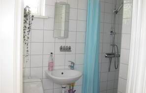 Un baño con lavamanos blanco, un espejo, ducha y ventana con planta.