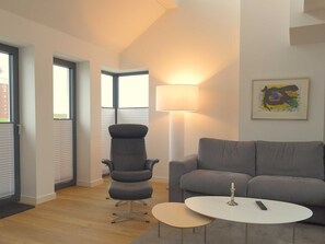 En moderne stue med en grå sofa, en sort lænestol, et lille hvidt bord og en gulvlampe.