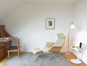 Et moderne værelse med skrivebord, stol, gulvlampe og et billede i ramme på væggen.
