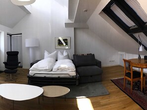 A modern loft bedroom with a large bed, a desk, and a dining table.