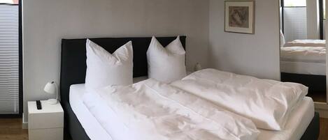 Una habitación de hotel moderna con una cama grande, una mesita de noche, una lámpara y una ventana con persianas.
