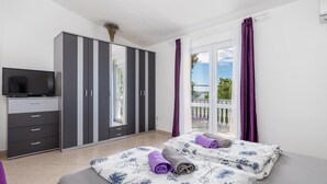 Un dormitorio con cama, televisión, armario y balcón con cortinas.