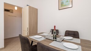 Un comedor con una mesa de madera dispuesta para cuatro personas, una botella de champán y dos copas. Hay sillas alrededor de la mesa y un cuadro en la pared.