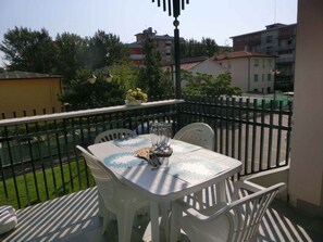 A balcony with a table and chairs, a flower vase, and a view of buildings and trees.