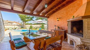 A covered outdoor area with a pool, wooden furniture, and a stone fireplace. - Amazing home in Boduleri (Boduleri)
