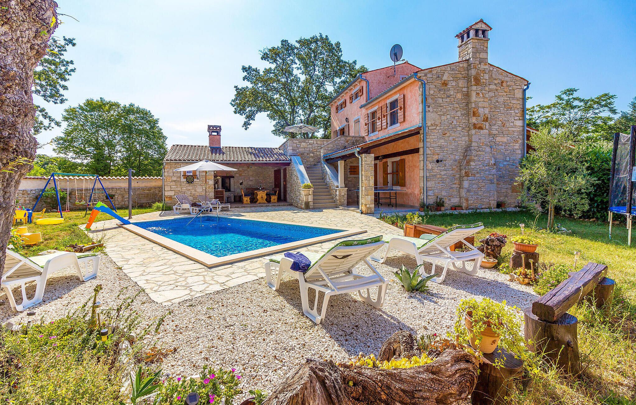 A stone house with a swimming pool, outdoor seating, and a children's play area.
