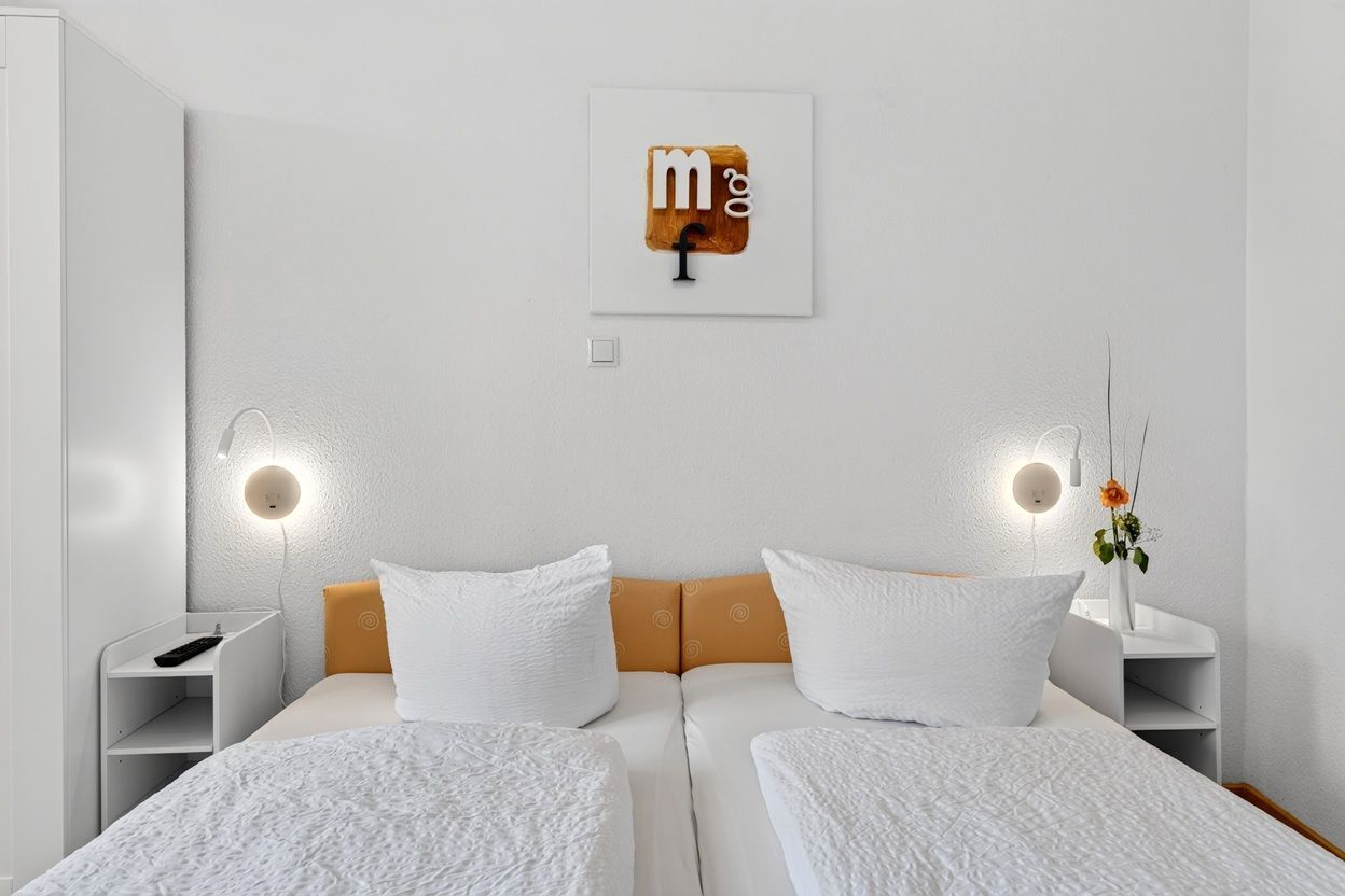 Quarto de hotel com duas camas, uma obra de arte na parede, abajures e uma pequena mesa com um vaso de flores.