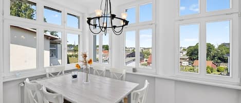 A dining room with a white table and chairs, large windows, and a chandelier.