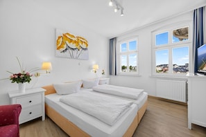 Ein Hotelzimmer mit Bett, Nachttischen, Lampen, einem Gemälde, einem Fenster mit Blick und einer Heizung.
