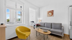 Una sala moderna con un sofá, un sillón amarillo, una mesa de centro y una ventana con cortinas.