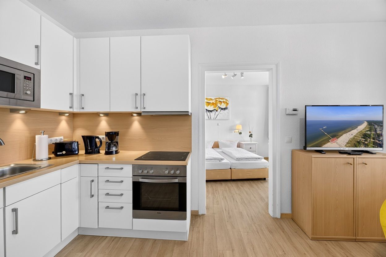 Una cocina moderna con armarios blancos, microondas integrado, estufa y cafetera.