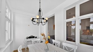 Un comedor con una mesa blanca, sillas, una araña y un florero con flores.