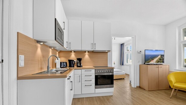 Cocina compacta con armarios blancos, horno integrado y cafetera.