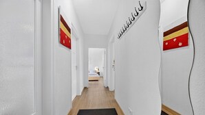 Un pasillo con una cama al final, un felpudo negro y una pared con una bandera.