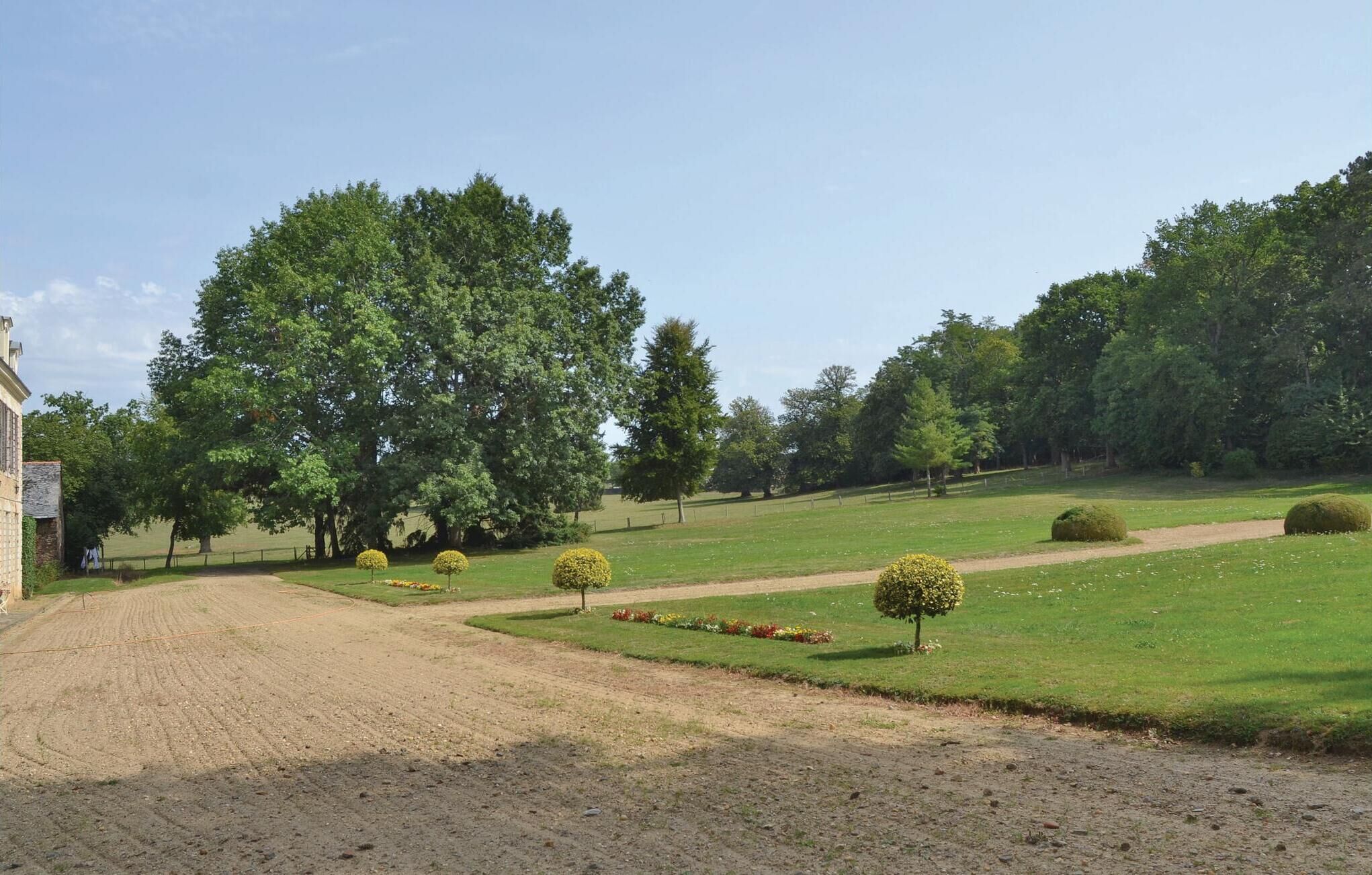 A rural landscape with a dirt path leading to a stone building, surrounded by lush greenery and neatly trimmed hedges.