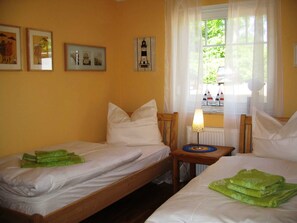 A room with two single beds, a small table with a lamp, and a window with a view of boats.