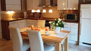A modern kitchen with white cabinets, a wooden countertop, a dining table with chairs, and a vase of flowers. - Herring Gull - Herring Gull (Heringsdorf)