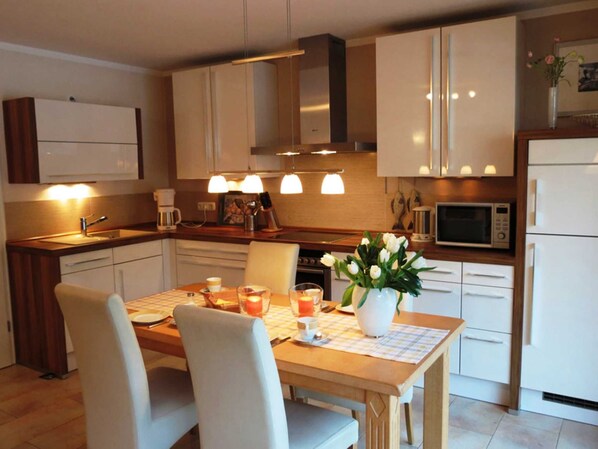 A modern kitchen with white cabinets, a wooden countertop, a dining table with chairs, and a vase of flowers.