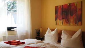 A hotel room with a bed, two pillows, a painting, a window with curtains, and a radiator. - Herring Gull - Herring Gull (Heringsdorf)
