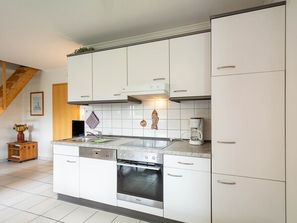 A modern kitchen with white cabinets, a stainless steel oven, a coffee maker, and a wooden stool. - Reriker Straße RER20-02. - Reriker Straße 20 Whg. 02 (Kühlungsborn)