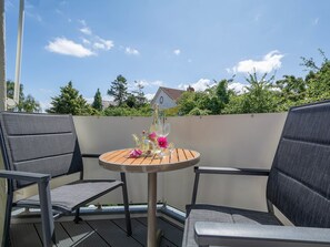 Une table ronde avec deux chaises sur un balcon, une bouteille de champagne et un verre posé sur la table.