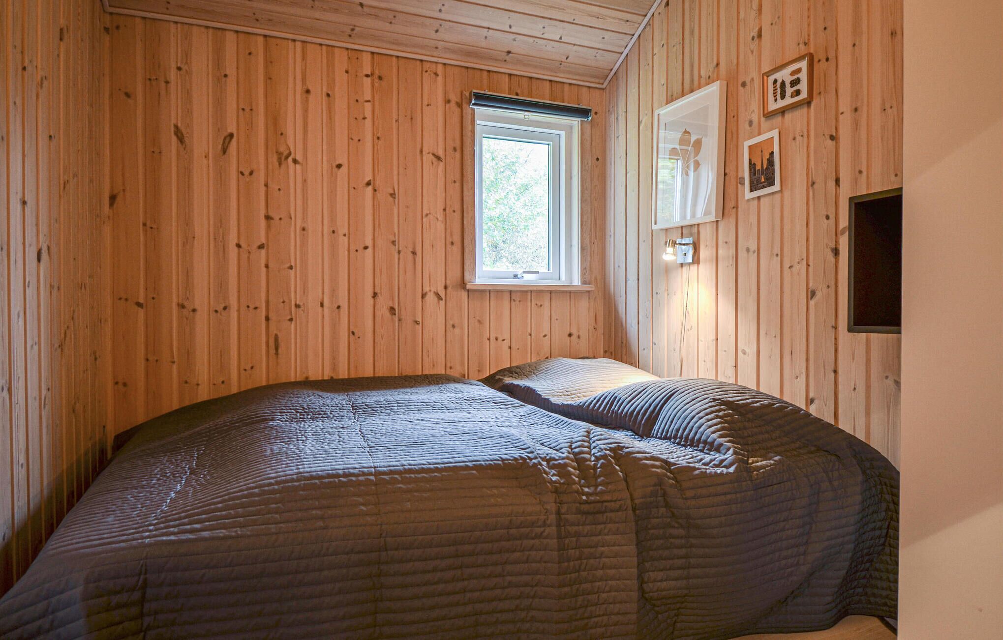 A bedroom with wooden paneling, a window, and a bed with a striped blanket.