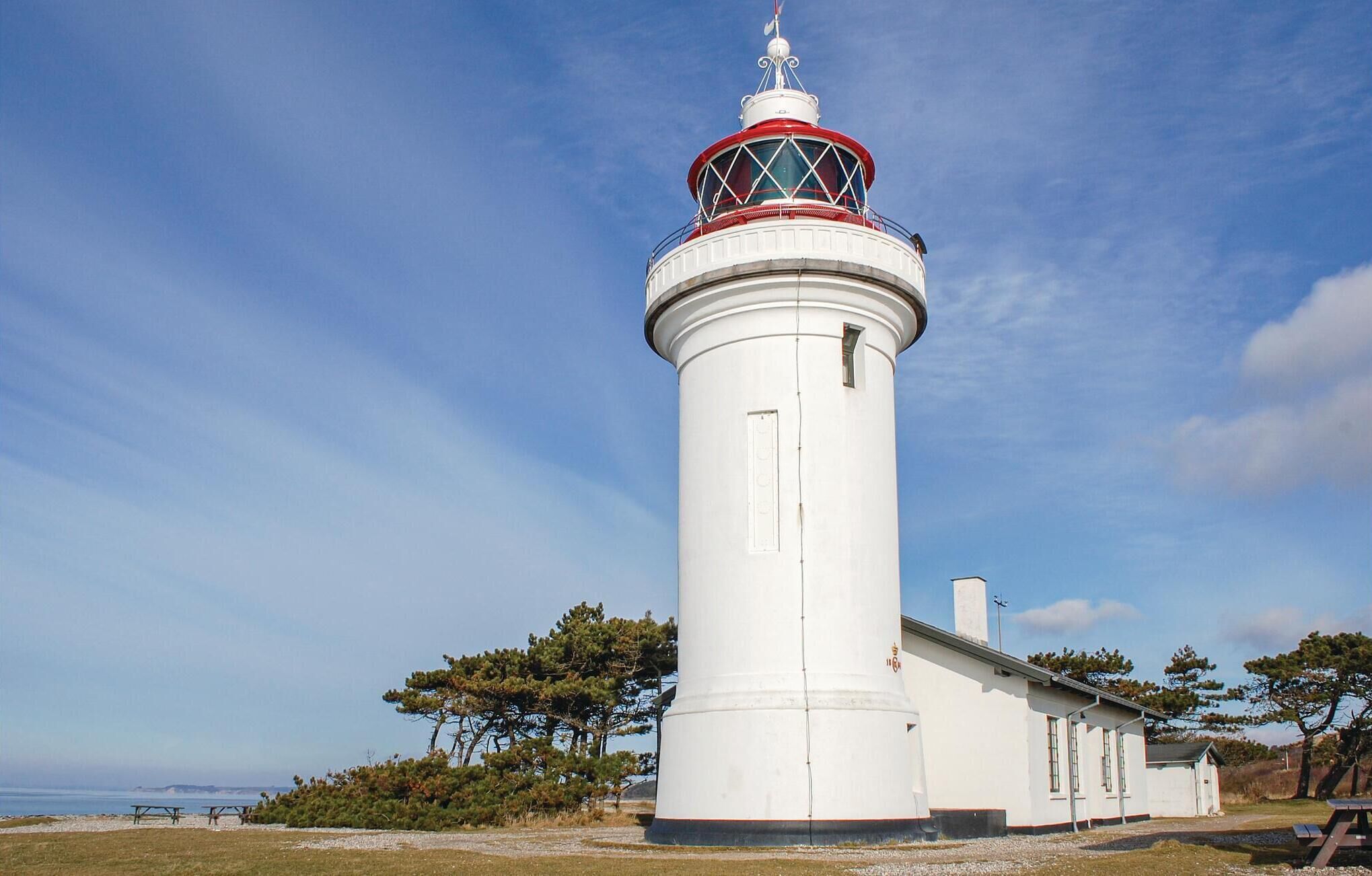 Een witte vuurtoren met een rood-wit top, gelegen op een grasveld met bomen en een heldere lucht.