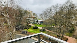 Blick vom Balkon auf einen Park mit Wegen, Bäumen und einem Gebäude im Hintergrund.