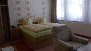 Un dormitorio con cama, una silla, una mesita de noche y un ventanal con cortinas.