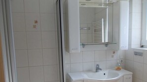 Un baño con cabina de ducha de vidrio, un lavamanos blanco con un solo grifo y un espejo sobre el lavamanos.