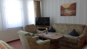 Una sala de estar con un sofá, dos sillones, una mesa de centro, un televisor y un cuadro en la pared.