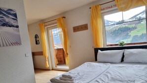 Ein Schlafzimmer mit Bett, einem Fenster mit Vorhängen, Blick ins Freie und einer kleinen Pflanze auf der Fensterbank.