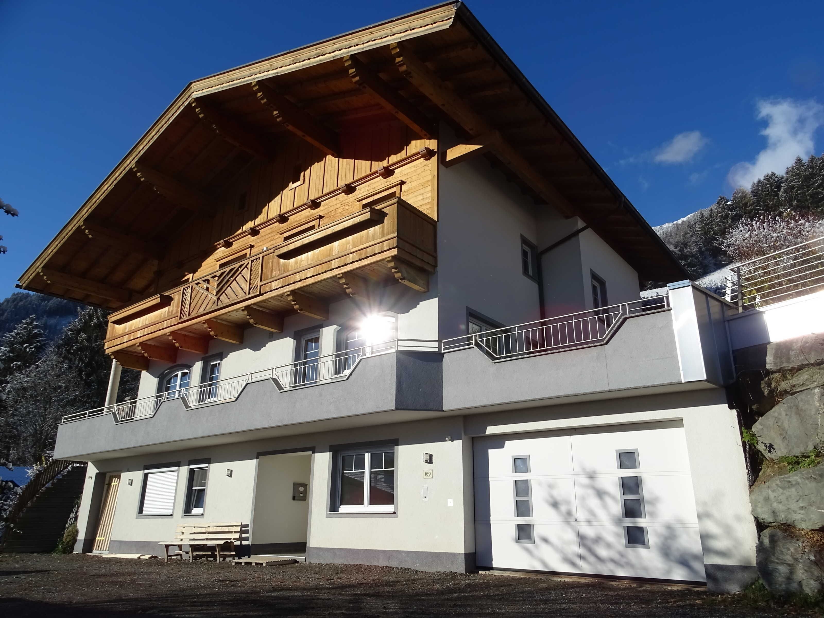 A two-story building with a wooden balcony, a bench, and a garage door.