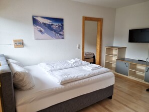 A bedroom with a bed, a television, a wardrobe, and a painting on the wall.