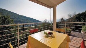 A balcony with a table covered in a yellow tablecloth, a vase with flowers, and a view of a mountainous landscape. - Cozy apartment in Moscenicka Draga (Moscenicka Draga)