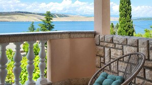 A balcony with a wicker chair and a view of a lake and hills.