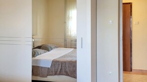 A bedroom with a bed, a window with curtains, and a door leading to another room.