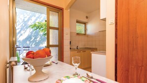 A kitchen with a window, a bowl of fruit, a wine glass, and a table set with a plate and utensils.