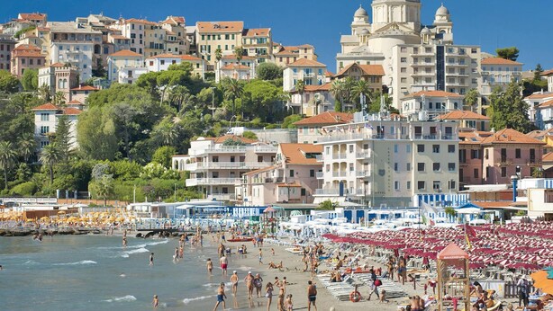 Eine Küstenstadt mit Strand, zahlreichen Sonnenschirmen und einem Hotel mit markantem Kuppelbau.