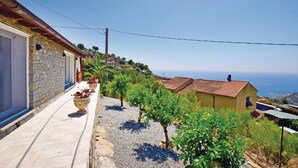 Ein Steinhaus mit Ziegeldach, einem Balkon mit Blumentöpfen und Blick auf das Meer.